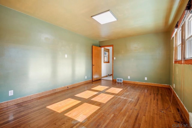 empty room featuring wood-type flooring, visible vents, and baseboards