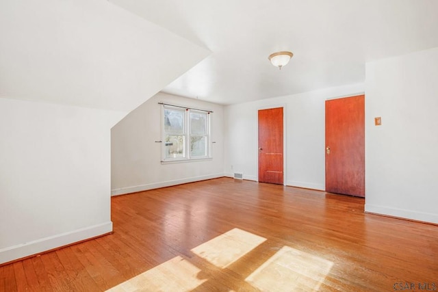 additional living space featuring vaulted ceiling, wood finished floors, visible vents, and baseboards