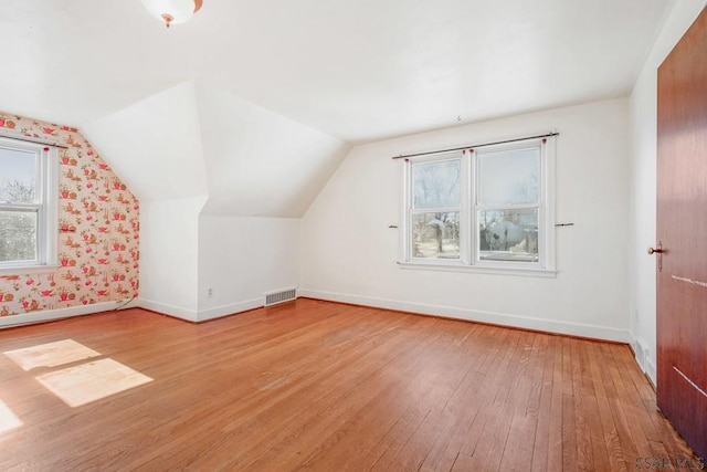 bonus room featuring light wood-type flooring, visible vents, vaulted ceiling, and baseboards