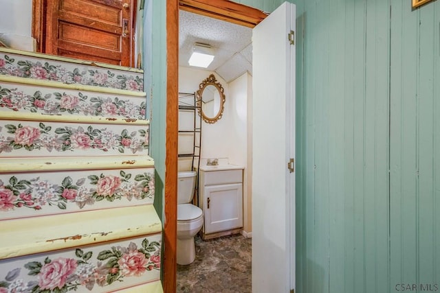 half bath with a textured ceiling, vanity, and toilet