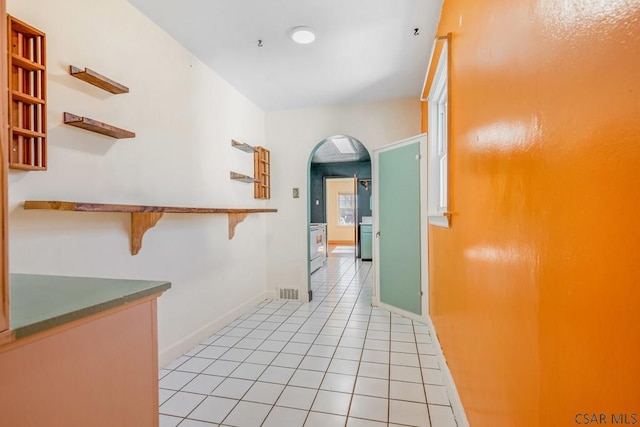 hall featuring light tile patterned floors, arched walkways, visible vents, and baseboards