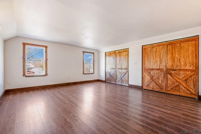 unfurnished bedroom with vaulted ceiling, baseboards, and dark wood finished floors