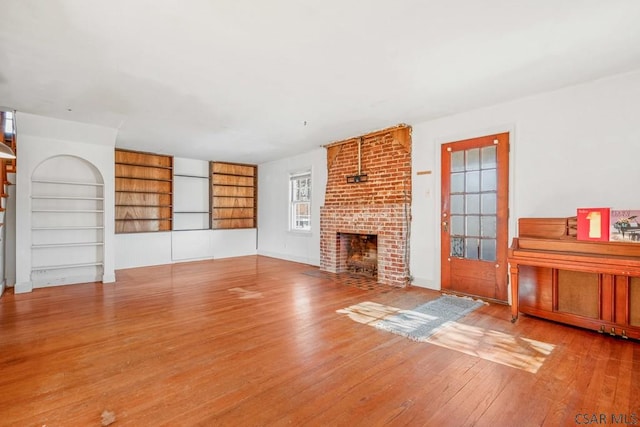 unfurnished living room featuring built in shelves, wood-type flooring, and a fireplace