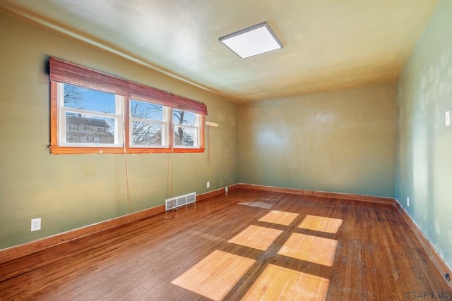 empty room featuring hardwood / wood-style flooring, visible vents, and baseboards