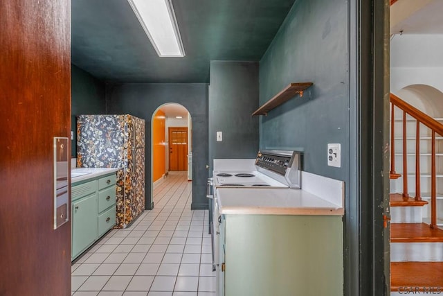 kitchen with arched walkways, light tile patterned floors, white range with electric cooktop, light countertops, and green cabinetry