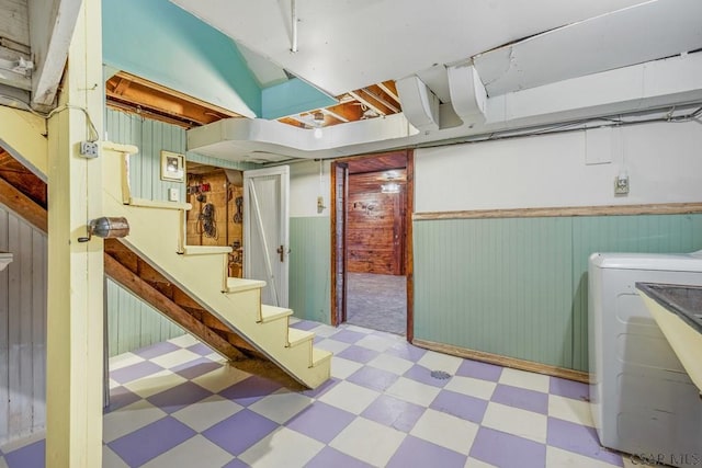 finished basement with a wainscoted wall, stairway, wood walls, washer / dryer, and tile patterned floors