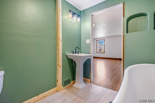 bathroom with visible vents, a freestanding bath, baseboards, and wood finished floors