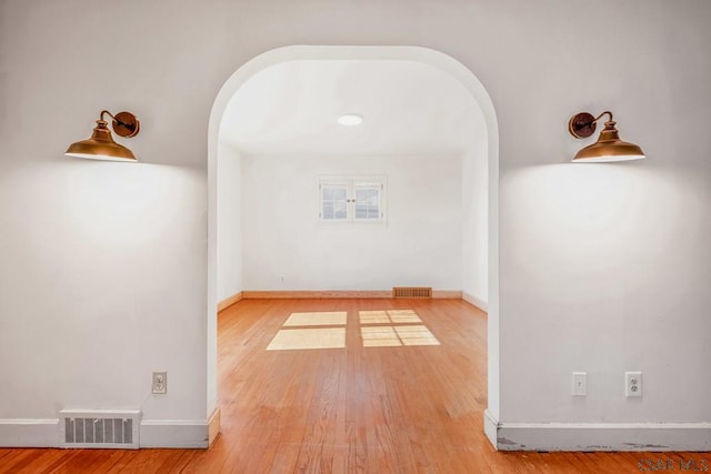 spare room featuring light wood-style flooring, visible vents, arched walkways, and baseboards