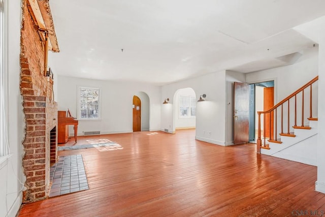 unfurnished living room with baseboards, visible vents, arched walkways, wood finished floors, and stairs