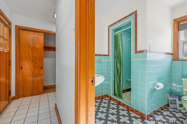 full bath with toilet, a stall shower, tile patterned flooring, and tile walls