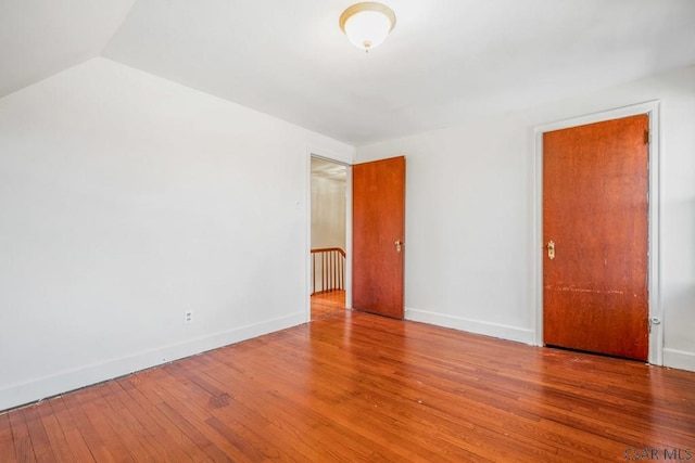 empty room with lofted ceiling, wood-type flooring, and baseboards