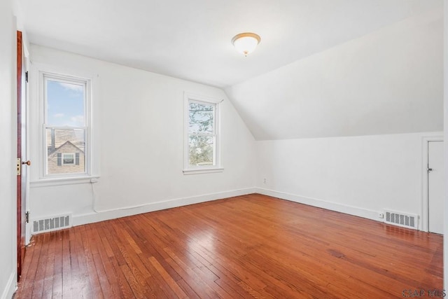 additional living space with vaulted ceiling, hardwood / wood-style flooring, visible vents, and baseboards