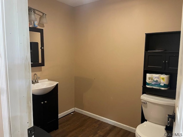 half bathroom with vanity, toilet, wood finished floors, and baseboards