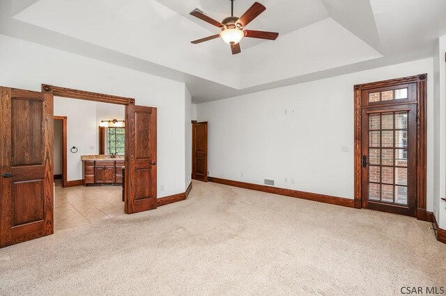 bedroom featuring a raised ceiling, light carpet, connected bathroom, and ceiling fan