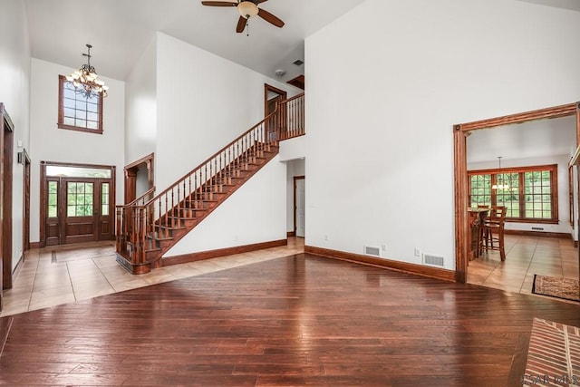 living room featuring wood-type flooring, a towering ceiling, and ceiling fan with notable chandelier