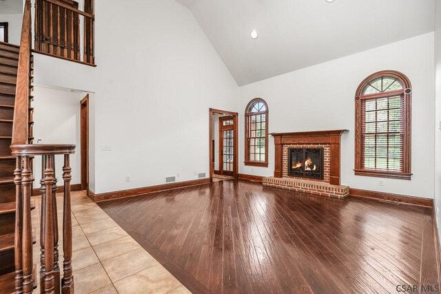 unfurnished living room featuring a brick fireplace, light tile patterned floors, high vaulted ceiling, and a healthy amount of sunlight