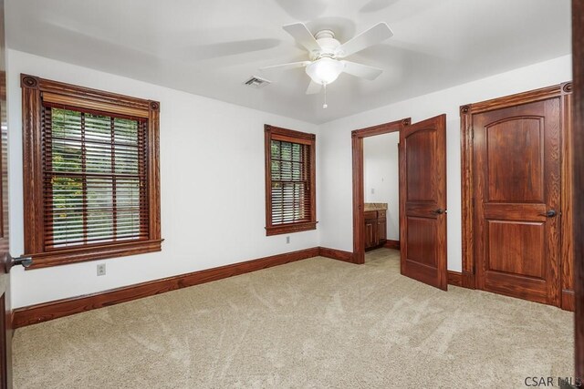 unfurnished bedroom featuring ensuite bathroom, light colored carpet, and ceiling fan