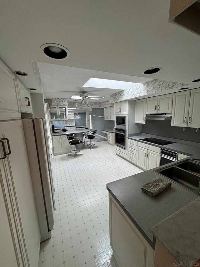 kitchen featuring sink, black appliances, a skylight, kitchen peninsula, and white cabinets