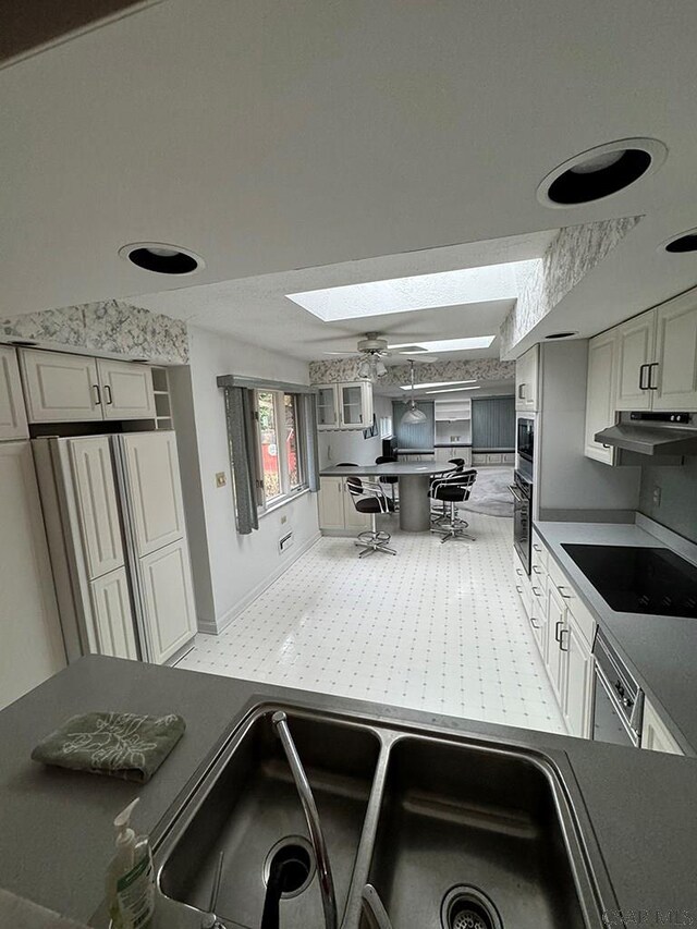 kitchen featuring sink, dishwasher, a skylight, black electric cooktop, and oven