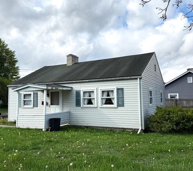 rear view of property featuring fence, a chimney, and a lawn