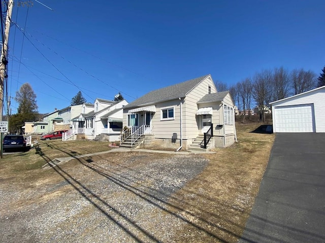 view of front facade with entry steps, a detached garage, an outdoor structure, and roof with shingles