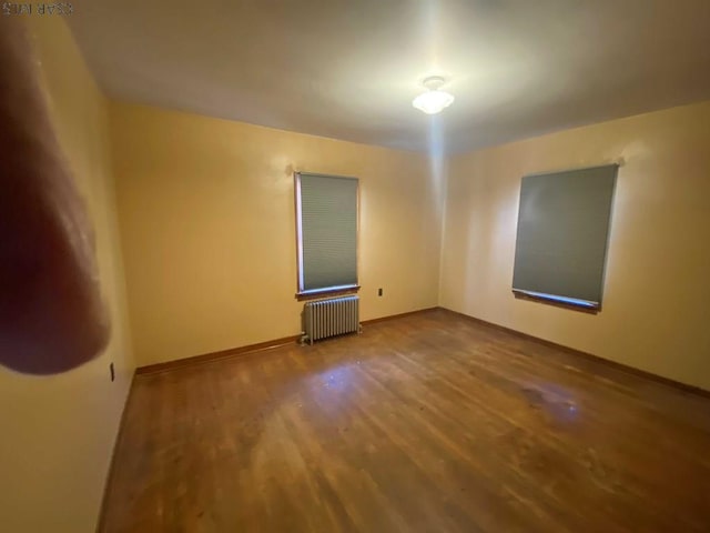 empty room with radiator, baseboards, and wood finished floors