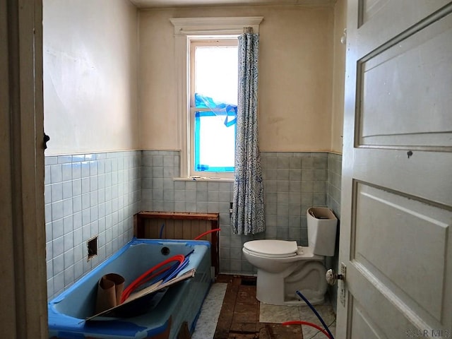 bathroom with a bathing tub, tile walls, and toilet