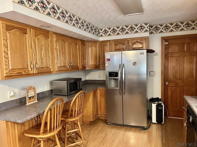 kitchen with appliances with stainless steel finishes, a kitchen bar, light hardwood / wood-style floors, and a textured ceiling