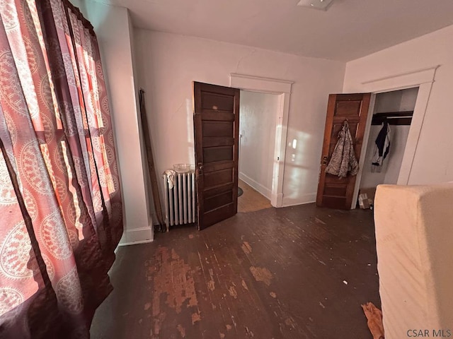 unfurnished bedroom featuring radiator heating unit, dark hardwood / wood-style flooring, and a closet