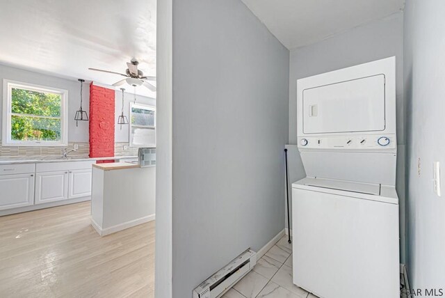 washroom with baseboard heating, ceiling fan, stacked washer and clothes dryer, and sink