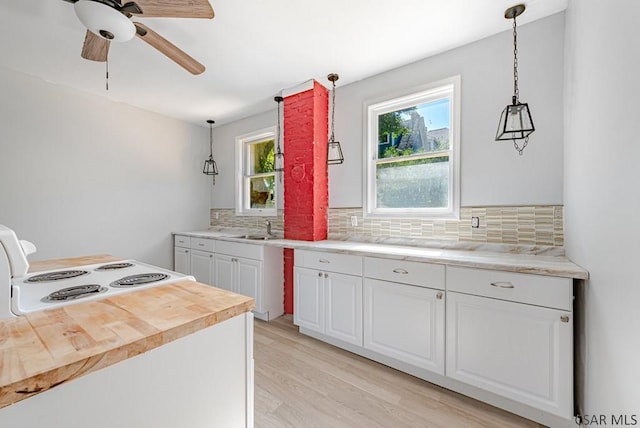 kitchen with tasteful backsplash, white cabinetry, sink, hanging light fixtures, and light wood-type flooring