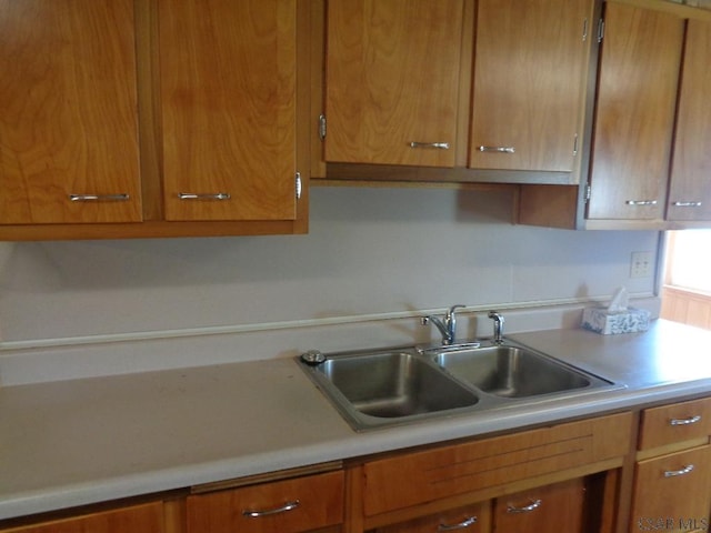 kitchen with brown cabinetry, light countertops, and a sink