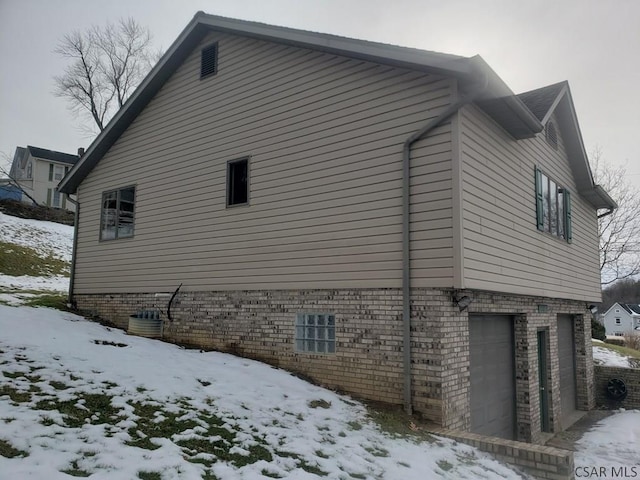 snow covered property with a garage and brick siding
