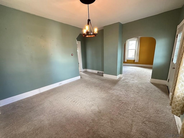 carpeted empty room featuring an inviting chandelier