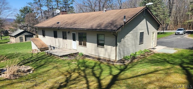 rear view of house featuring a shingled roof, a yard, and a chimney