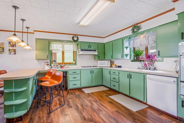 kitchen with white appliances, a peninsula, crown molding, under cabinet range hood, and dark wood finished floors