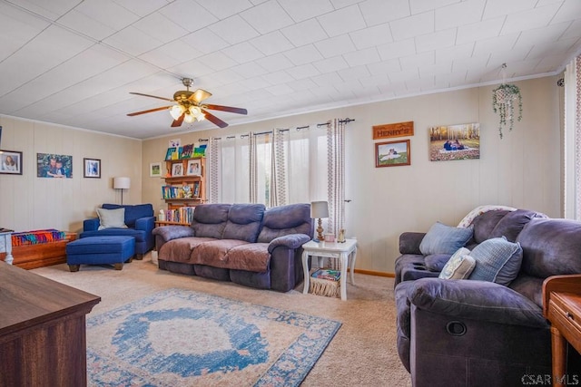 carpeted living area with ceiling fan, baseboards, and ornamental molding