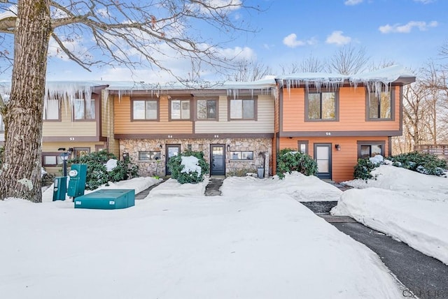 snow covered rear of property featuring stone siding