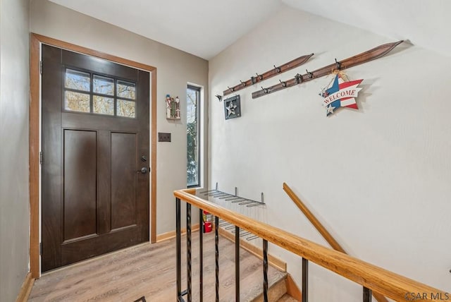 entryway featuring light wood-type flooring, stairway, baseboards, and vaulted ceiling