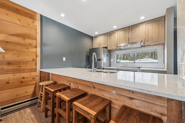 kitchen with light stone counters, a breakfast bar area, light brown cabinetry, freestanding refrigerator, and a sink