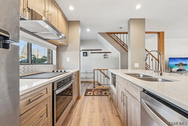 kitchen featuring light wood finished floors, a sink, stainless steel appliances, light brown cabinetry, and backsplash