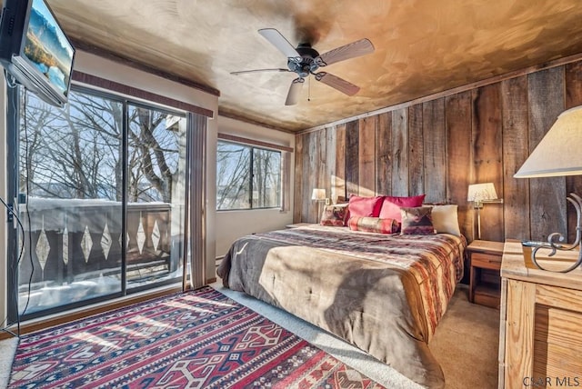 bedroom featuring access to exterior, carpet, wooden walls, and a ceiling fan