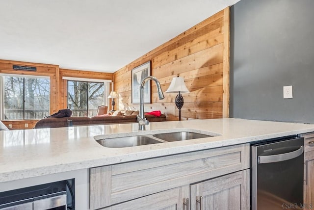 kitchen with stainless steel dishwasher, open floor plan, a sink, wooden walls, and beverage cooler