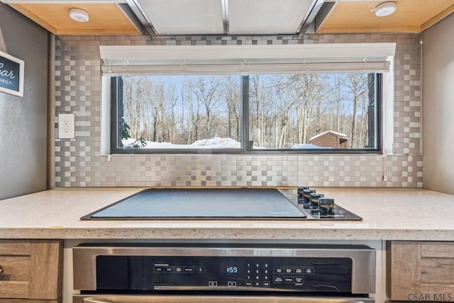 kitchen featuring light stone counters, stainless steel oven, black electric cooktop, and backsplash