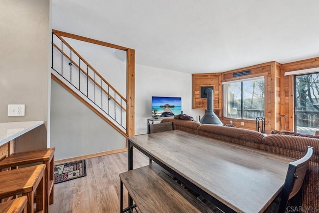 living room with light wood-style floors, a wood stove, stairway, and baseboards