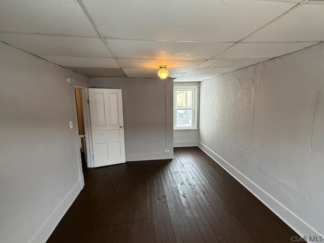 unfurnished room with a paneled ceiling, dark wood-style flooring, and baseboards