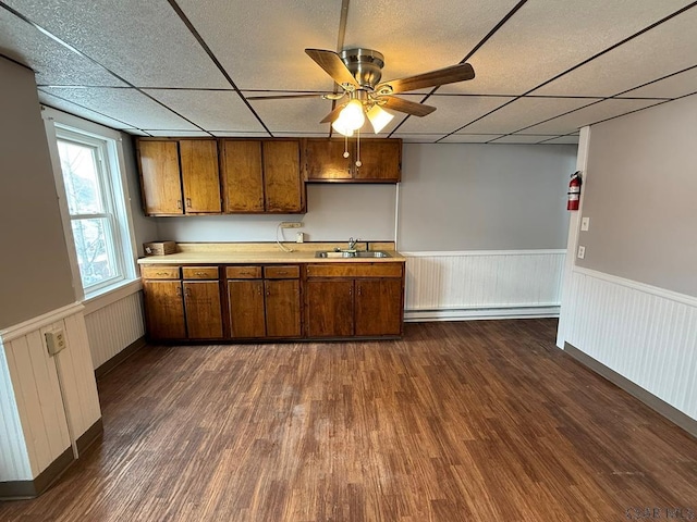 kitchen featuring light countertops, wainscoting, a baseboard radiator, and a drop ceiling