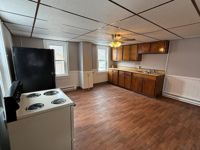 kitchen featuring light countertops, wainscoting, freestanding refrigerator, brown cabinets, and dark wood-style floors