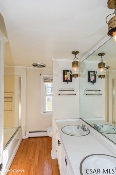 full bathroom with shower / bath combination with glass door, hardwood / wood-style floors, vanity, ornamental molding, and a baseboard radiator