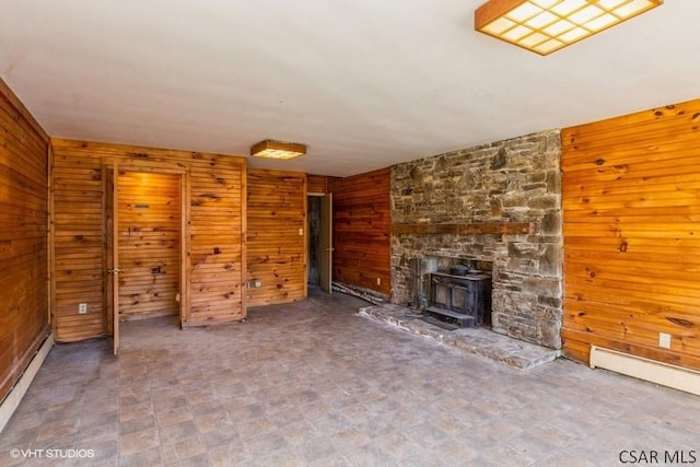 unfurnished living room with a baseboard radiator, a wood stove, and wooden walls